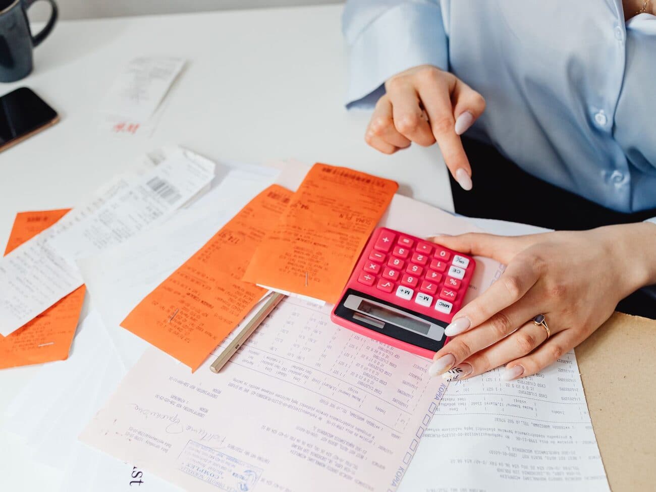 Mâinile unui contabil cu bonuri fiscale și un calculator de birou, deasupra unor documente.